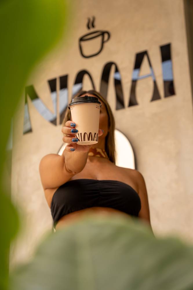 Café para llevar de Nimai frente al mural de la marca